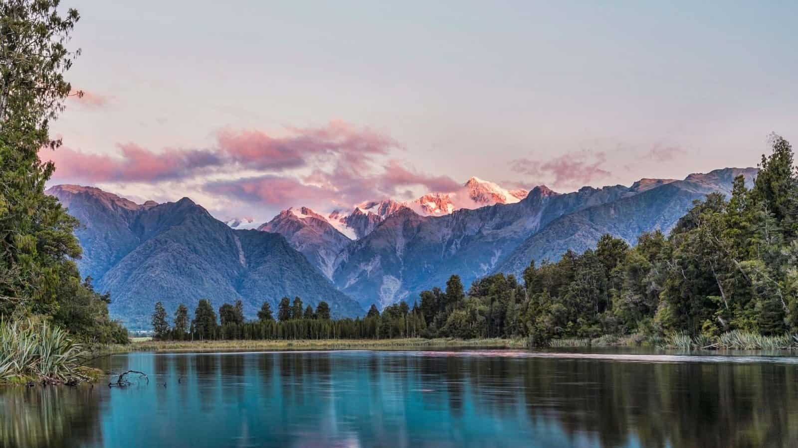 Breathtaking view of snow-capped mountains reflecting on a calm river surrounded by lush greenery. P.