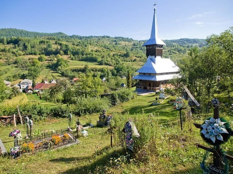 Church in a rural village with lush greenery, hills, and a bright sunny sky.