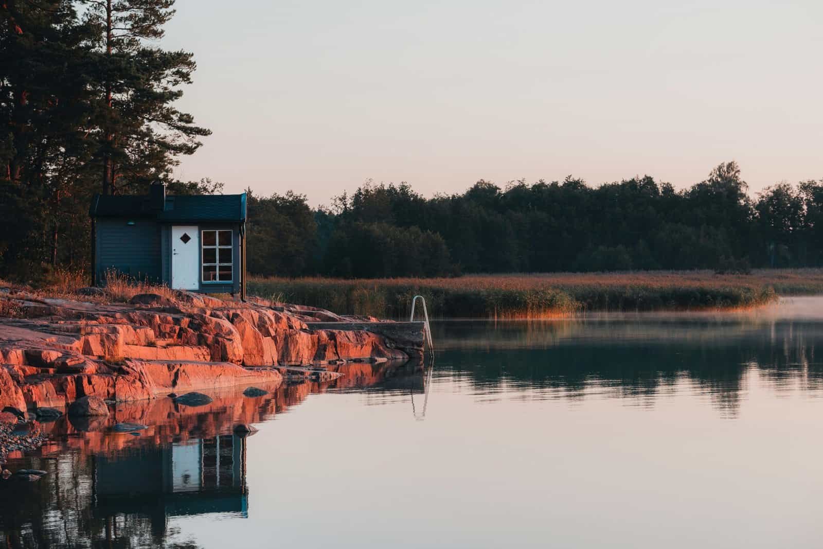 A small cabin on pink granite rocks by calm water, Aland Islands