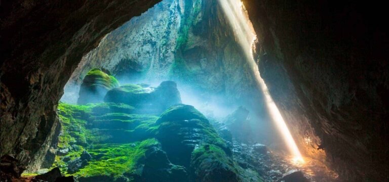 Sunlight falls through a collapsed ceiling into Son Doong cave, Vietnam, lighting moss-covered rock